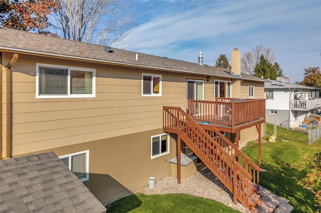 back of property with a lawn, a deck, fence, stairway, and roof with shingles