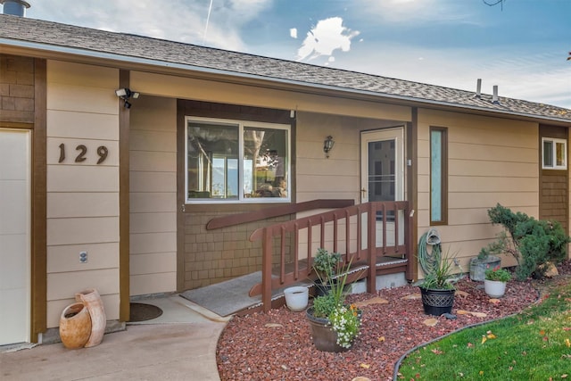 entrance to property with covered porch and a shingled roof