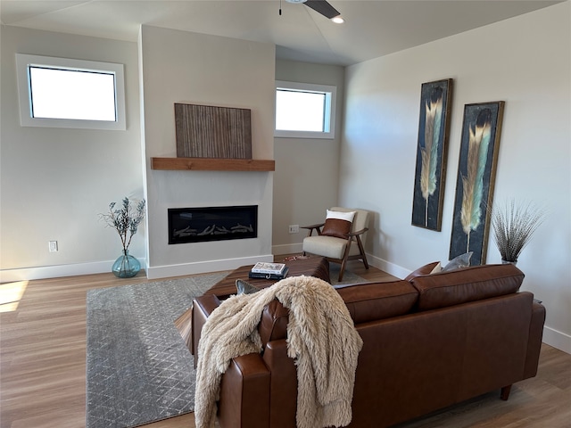 living area featuring a glass covered fireplace, a ceiling fan, baseboards, and wood finished floors