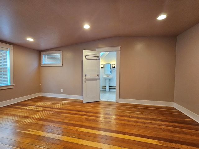 spare room with baseboard heating, wood-type flooring, and vaulted ceiling