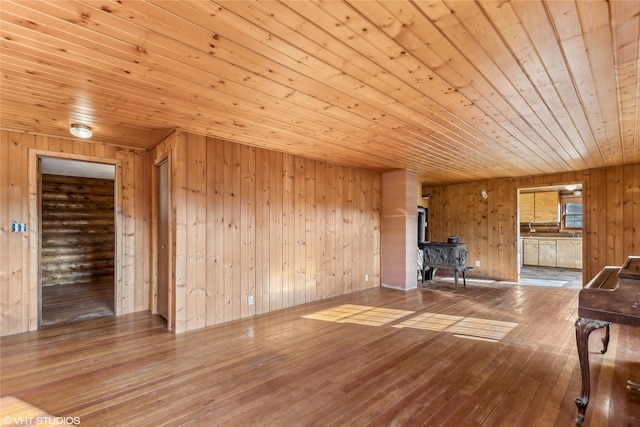 unfurnished living room featuring wooden walls, wood ceiling, wood-type flooring, and a wood stove