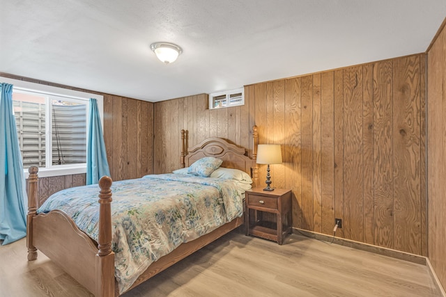 bedroom featuring wood walls, light hardwood / wood-style floors, and a textured ceiling