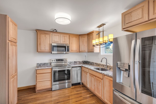 kitchen featuring stainless steel appliances, light stone countertops, hanging light fixtures, sink, and light hardwood / wood-style flooring