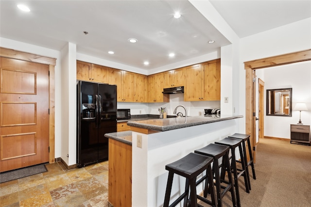 kitchen featuring a kitchen bar, kitchen peninsula, black appliances, sink, and dark stone countertops