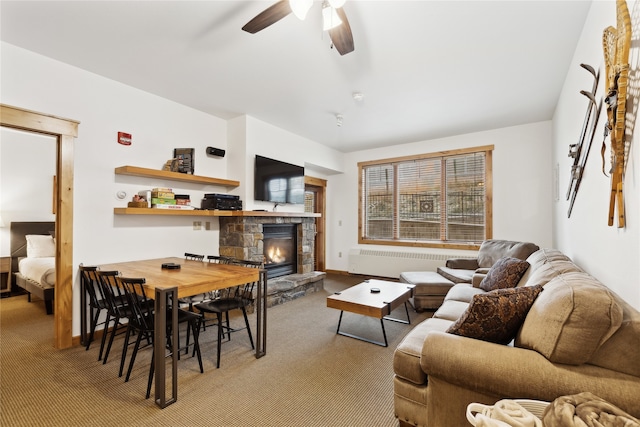 carpeted living room with a stone fireplace, ceiling fan, and radiator