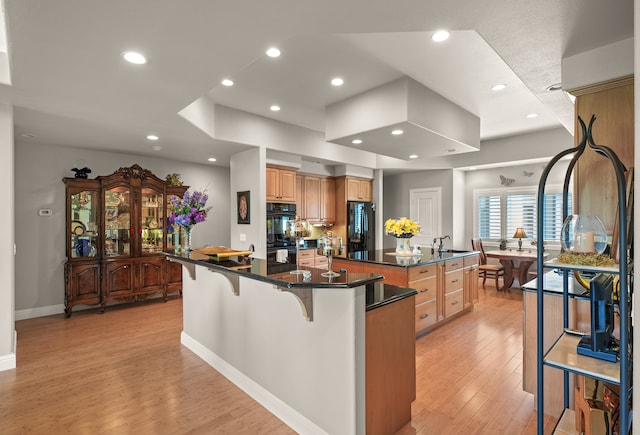 kitchen featuring black appliances, a breakfast bar, light hardwood / wood-style floors, and a center island