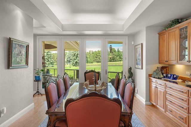 dining room with light wood-type flooring and a raised ceiling