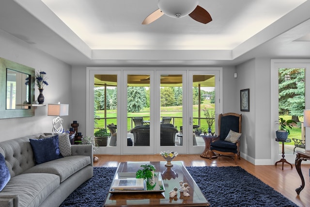 living room featuring a wealth of natural light, ceiling fan, a raised ceiling, and light wood-type flooring