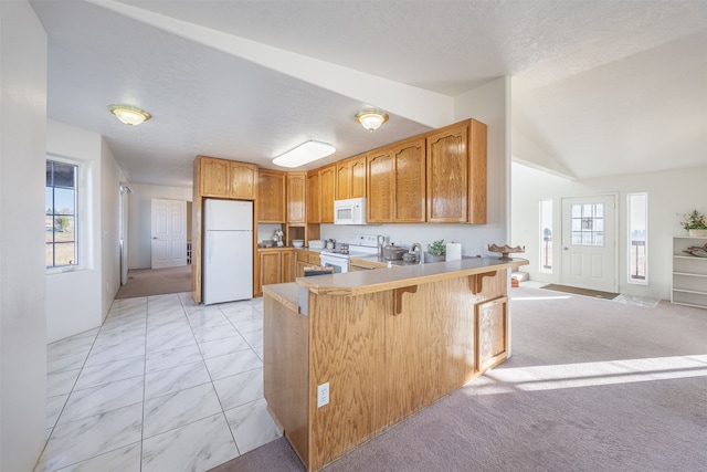 kitchen with kitchen peninsula, white appliances, a kitchen bar, lofted ceiling, and light colored carpet