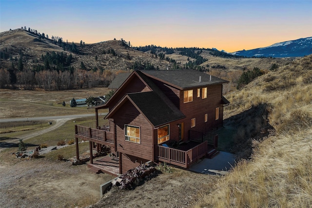 back house at dusk with a deck with mountain view