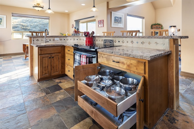 kitchen featuring plenty of natural light, light stone counters, sink, and decorative light fixtures