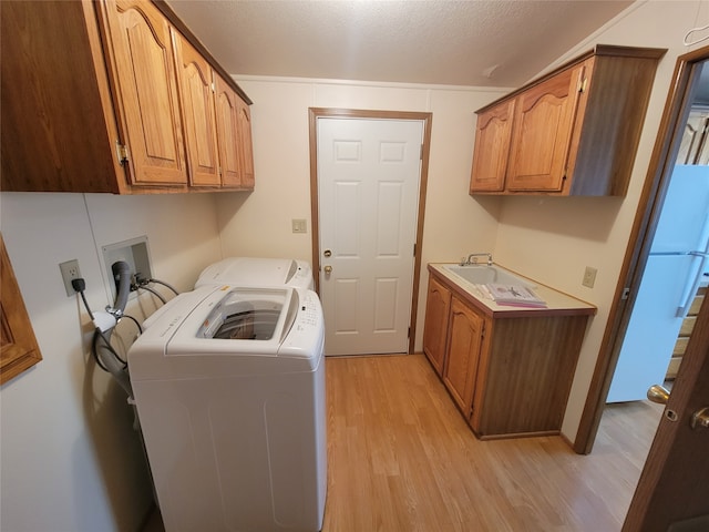 laundry area featuring washer and clothes dryer, light wood-type flooring, cabinets, and a textured ceiling