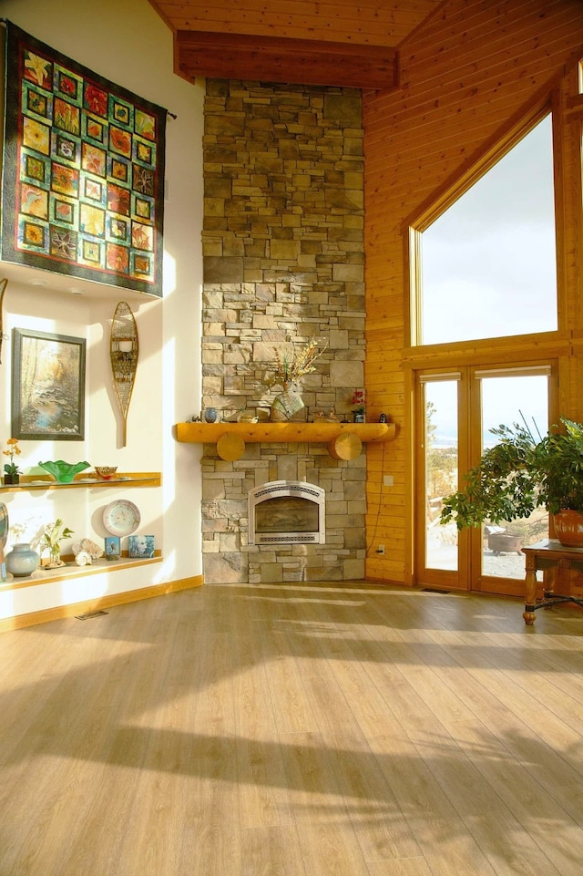 living room with a stone fireplace, a towering ceiling, wood walls, and hardwood / wood-style flooring