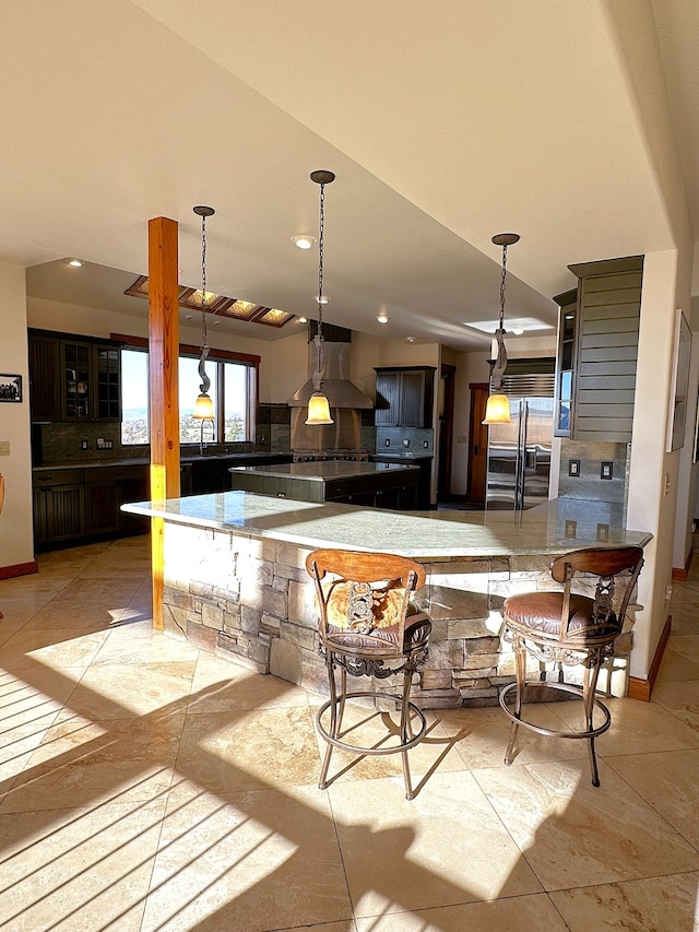 kitchen featuring built in refrigerator, kitchen peninsula, hanging light fixtures, island exhaust hood, and a breakfast bar