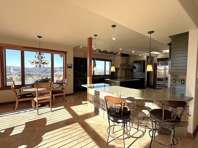 kitchen featuring wall chimney exhaust hood, a healthy amount of sunlight, kitchen peninsula, and built in refrigerator