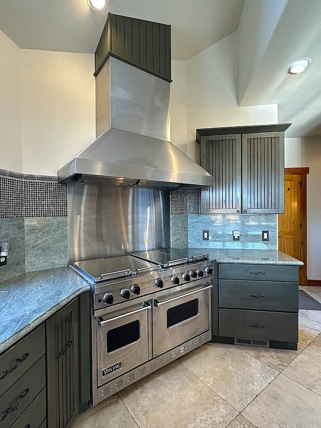 kitchen with wall chimney exhaust hood, range with two ovens, light stone counters, and tasteful backsplash