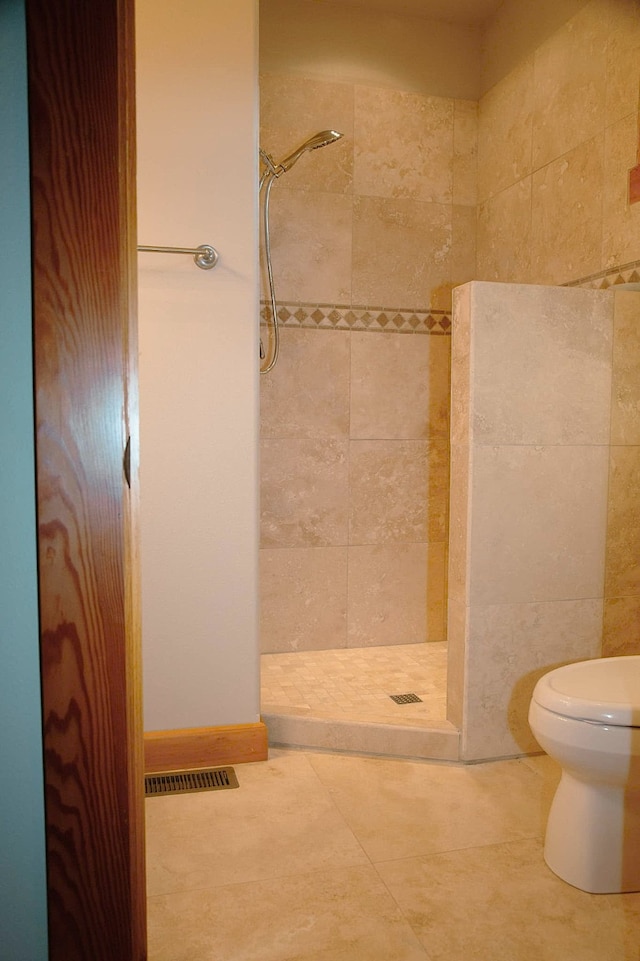 bathroom with toilet, tile patterned floors, and a tile shower