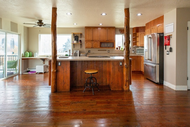 kitchen with a kitchen breakfast bar, ceiling fan, a textured ceiling, appliances with stainless steel finishes, and dark hardwood / wood-style flooring