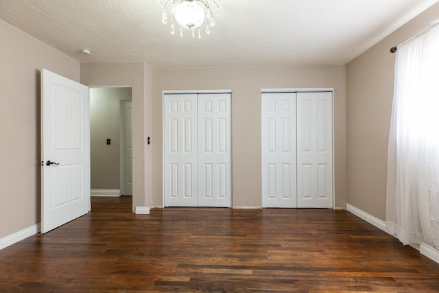 unfurnished bedroom with a textured ceiling, dark hardwood / wood-style floors, and multiple closets