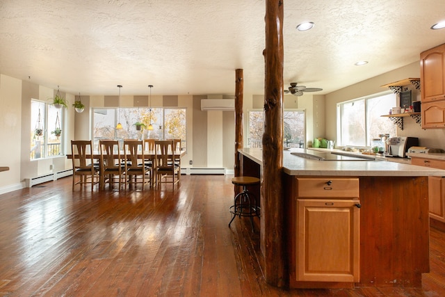 kitchen with pendant lighting, dark hardwood / wood-style flooring, baseboard heating, and a wall unit AC