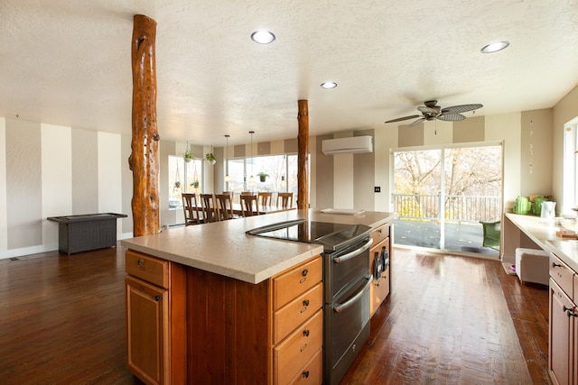 kitchen featuring an AC wall unit, an island with sink, a healthy amount of sunlight, and stainless steel electric range