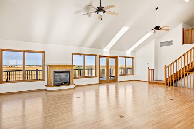 451 1st Rd NE, Fairfield, MT 59436 - unfurnished living room with high vaulted ceiling, ceiling fan, light wood-style floors, a tiled fireplace, and stairs
