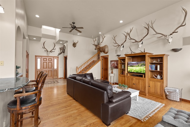 living room with ceiling fan, light hardwood / wood-style floors, and a towering ceiling