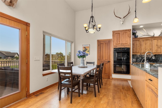 dining area featuring an inviting chandelier, sink, light wood-type flooring, and high vaulted ceiling