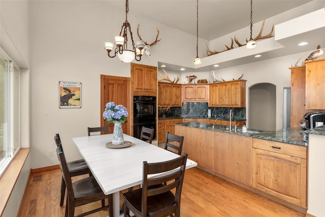 kitchen with tasteful backsplash, light wood-type flooring, decorative light fixtures, high vaulted ceiling, and double oven