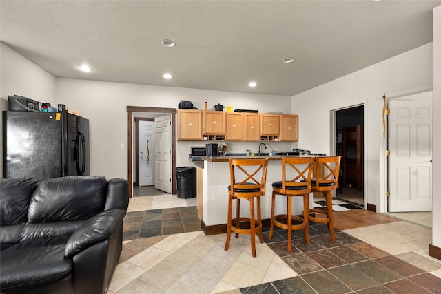 kitchen with a kitchen breakfast bar, sink, kitchen peninsula, and black fridge with ice dispenser