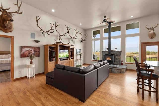 living room with a towering ceiling, ceiling fan, light wood-type flooring, and a wood stove