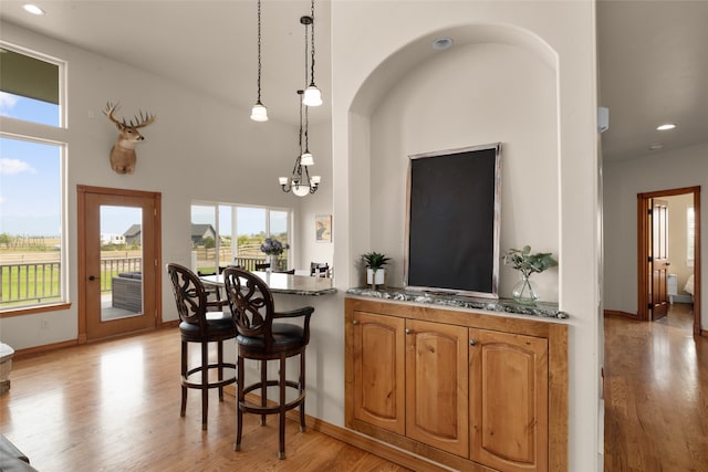 kitchen featuring a high ceiling, a breakfast bar, an inviting chandelier, hanging light fixtures, and light hardwood / wood-style flooring