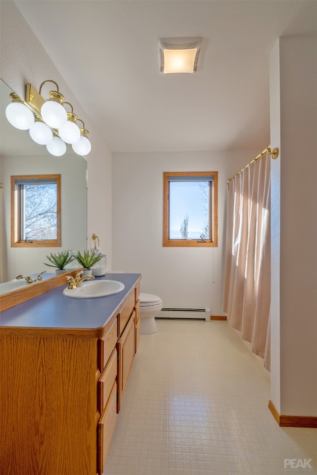 bathroom with a baseboard heating unit, a wealth of natural light, vanity, and toilet