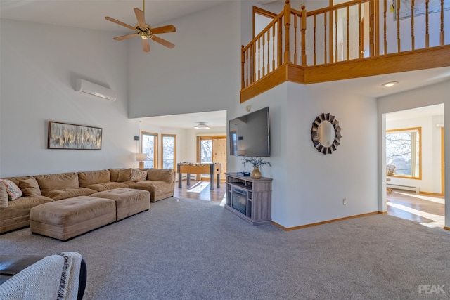 carpeted living room featuring a wall mounted AC, a towering ceiling, baseboard heating, and ceiling fan