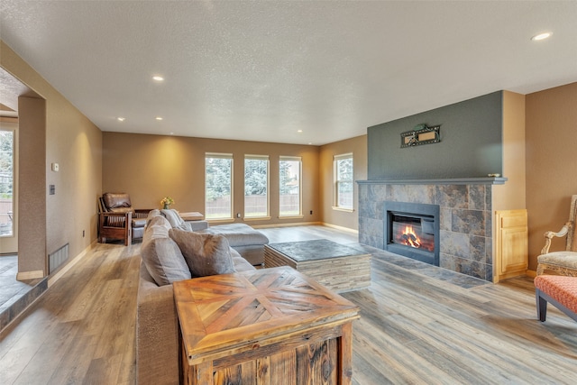 living room with a tiled fireplace, a textured ceiling, and light hardwood / wood-style flooring