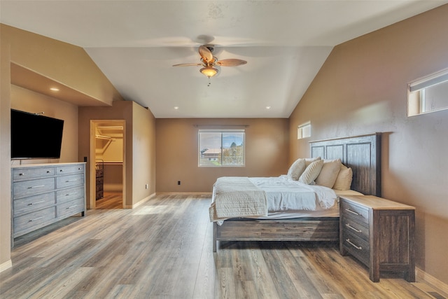 bedroom with ceiling fan, a walk in closet, vaulted ceiling, and light hardwood / wood-style floors