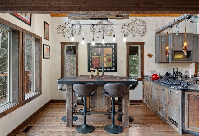 bar featuring stainless steel microwave, wood finished floors, a wealth of natural light, and baseboards