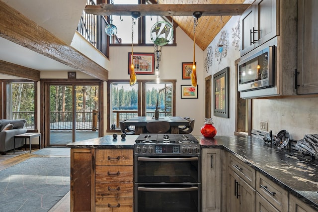 kitchen featuring beam ceiling, stone tile flooring, appliances with stainless steel finishes, open floor plan, and dark stone counters