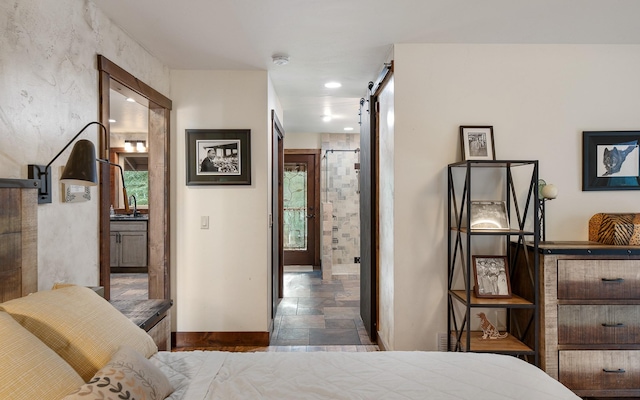 bedroom featuring a barn door, baseboards, ensuite bath, stone finish floor, and a sink