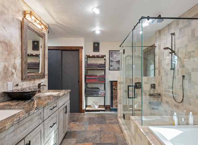 full bathroom featuring double vanity, a relaxing tiled tub, stone tile flooring, a shower stall, and a sink