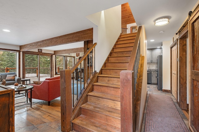 staircase featuring beam ceiling, recessed lighting, a barn door, wood finished floors, and baseboards