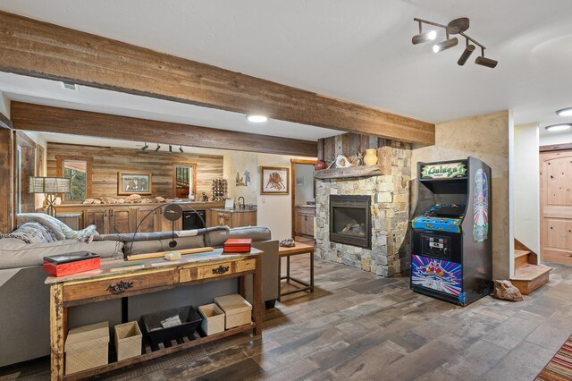 living area featuring beam ceiling, dark wood finished floors, visible vents, wooden walls, and a stone fireplace