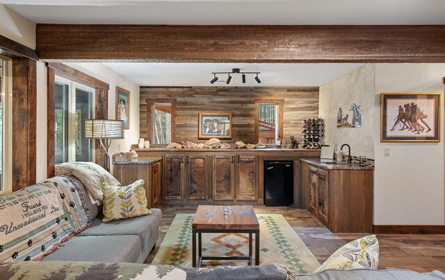 interior space with wet bar, beamed ceiling, baseboards, and wood finished floors