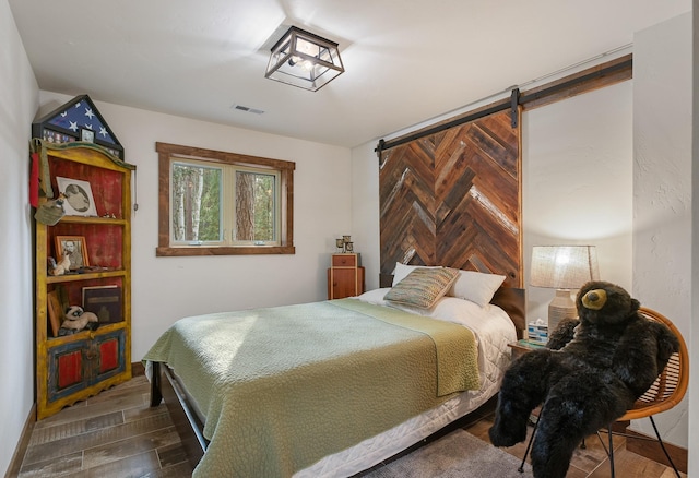 bedroom featuring a barn door, visible vents, dark wood finished floors, and baseboards