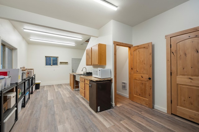 kitchen featuring wood finished floors, light countertops, a sink, and white microwave