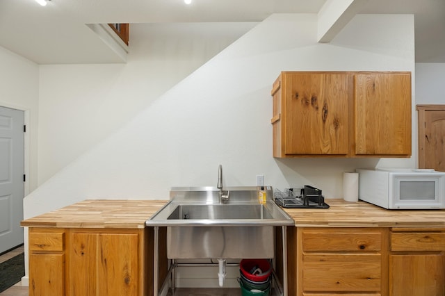 kitchen with butcher block counters, brown cabinets, a sink, and white microwave