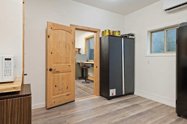 interior space featuring light wood-style floors, baseboards, white microwave, and a wall mounted AC