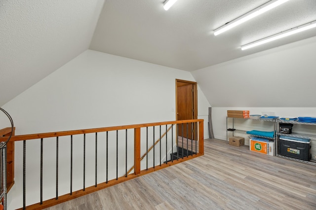 bonus room featuring light wood-type flooring, lofted ceiling, and a textured ceiling