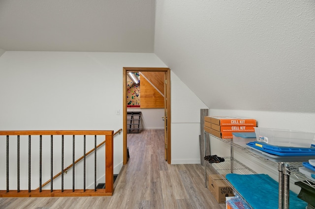 bonus room featuring vaulted ceiling, a textured ceiling, baseboards, and light wood-style floors