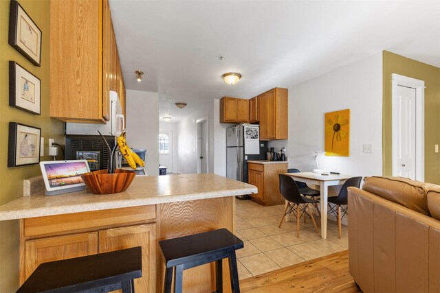 kitchen featuring kitchen peninsula, a kitchen bar, stainless steel fridge, and light hardwood / wood-style flooring